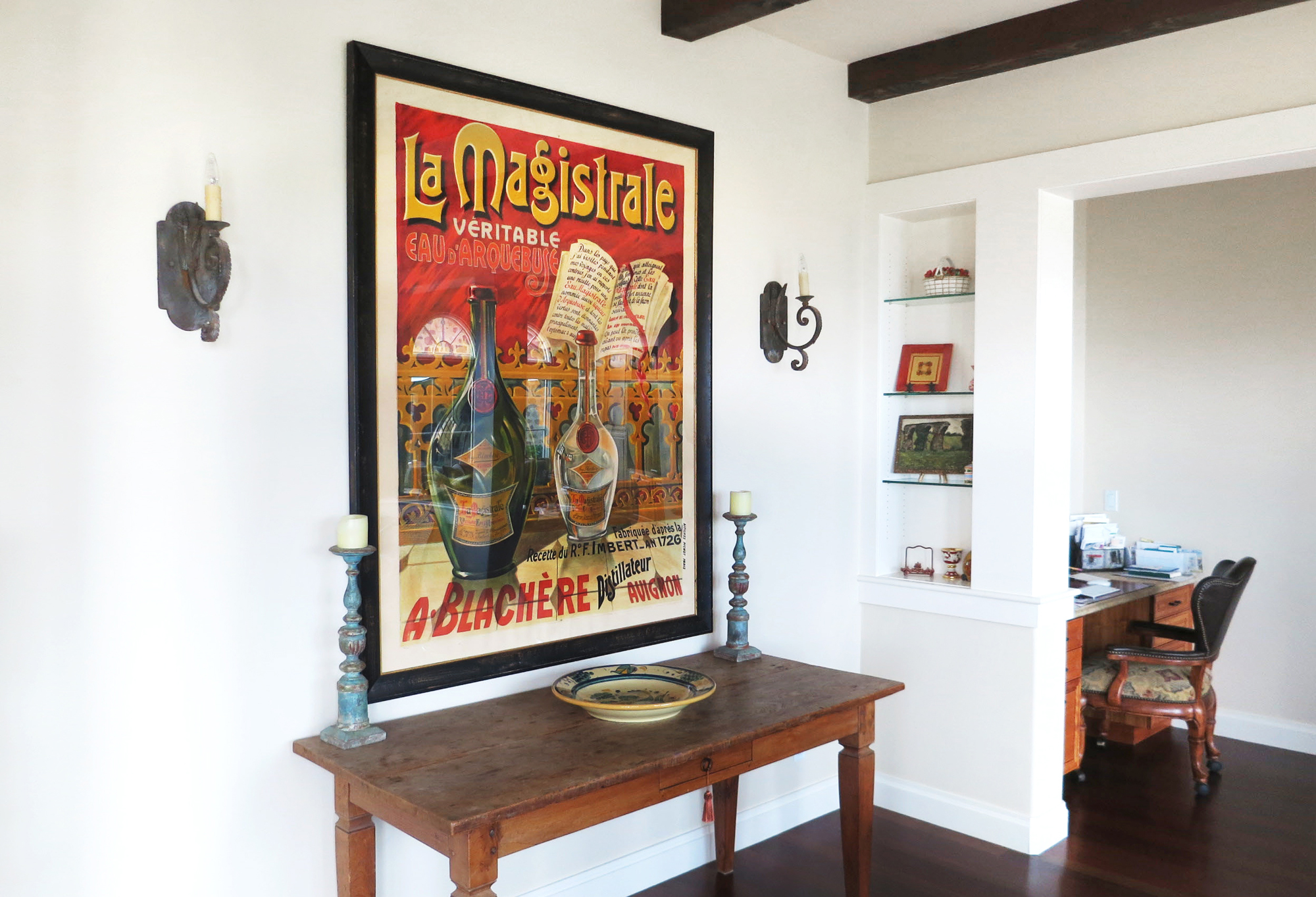 Ornate poster with bottle above farmhouse table; red, brown, white