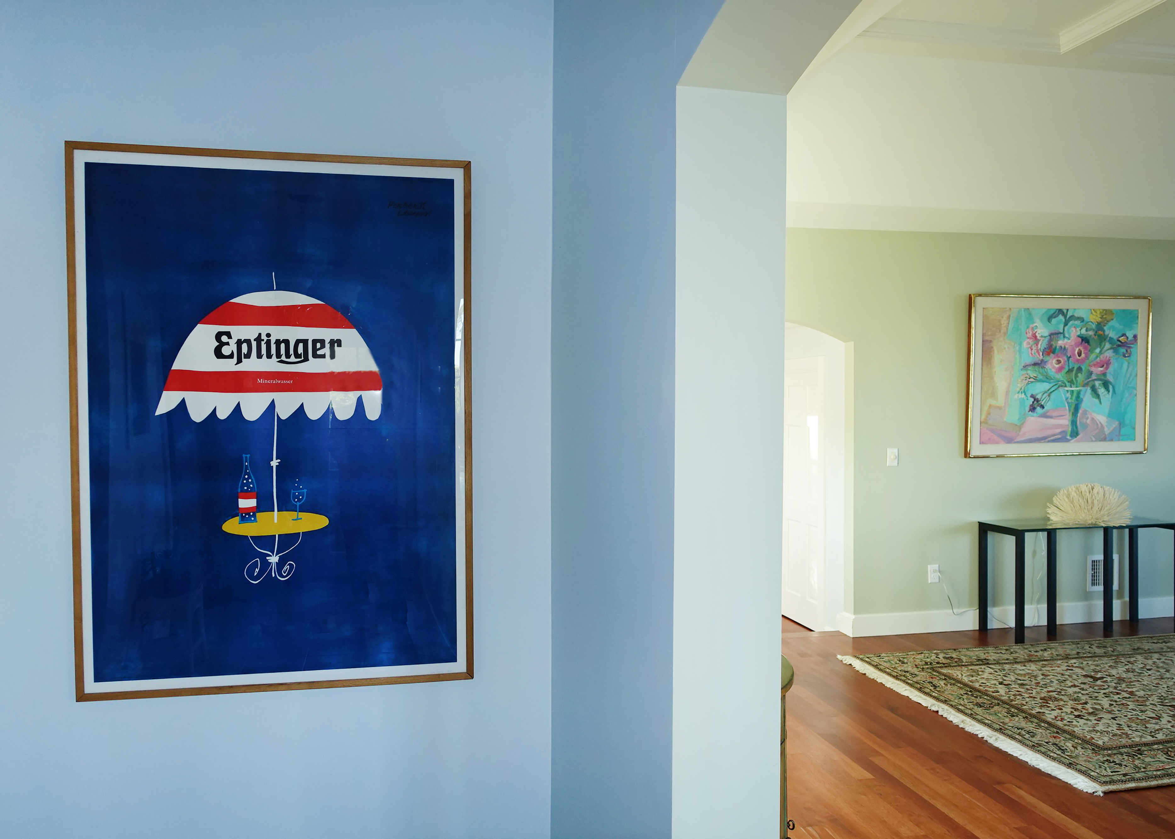 hallway with view into next room and Eptinger poster with striped umbrella; blue, red, yellow, green