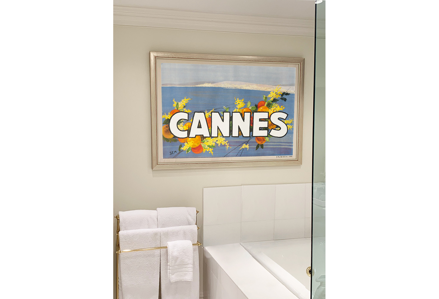 white bathroom with framed Cannes poster on wall; white, blue, orange, yellow